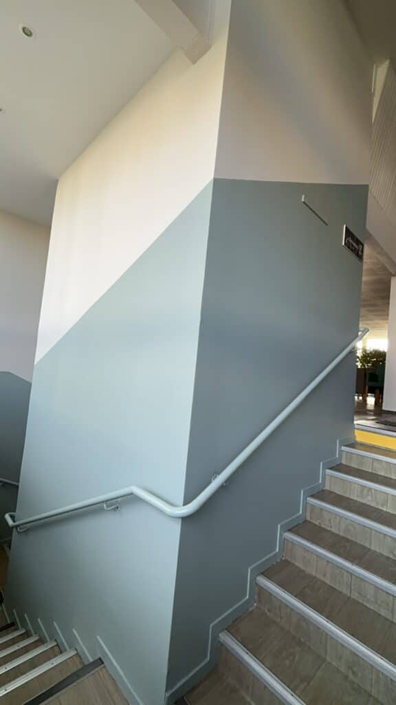 Escalier intérieur design: murs bicolores, main courante moderne Escalier intérieur moderne avec murs gris-bleu et blanc cassé en diagonale. Main courante blanche et marches bois. Signalétique murale.